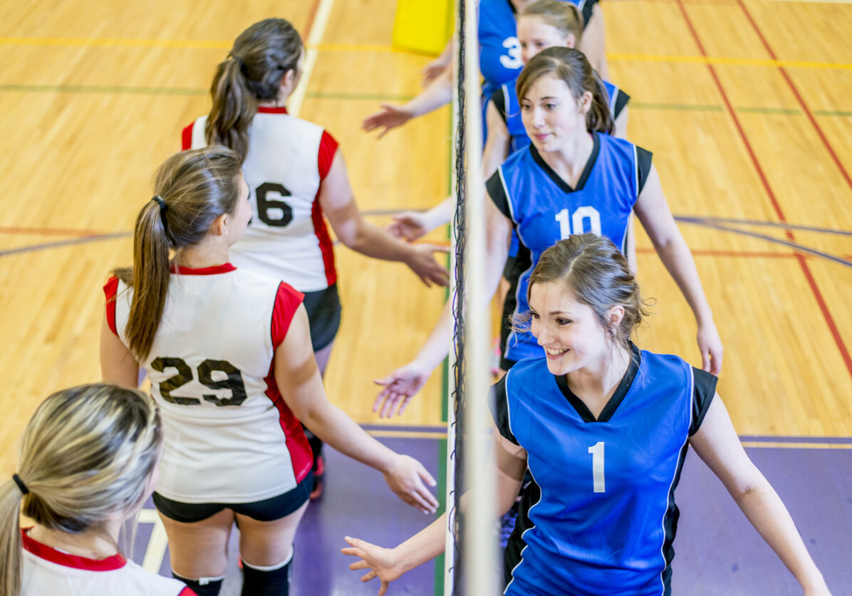 Group of teenage girls smiling and congratulating each other after a volleyball game.