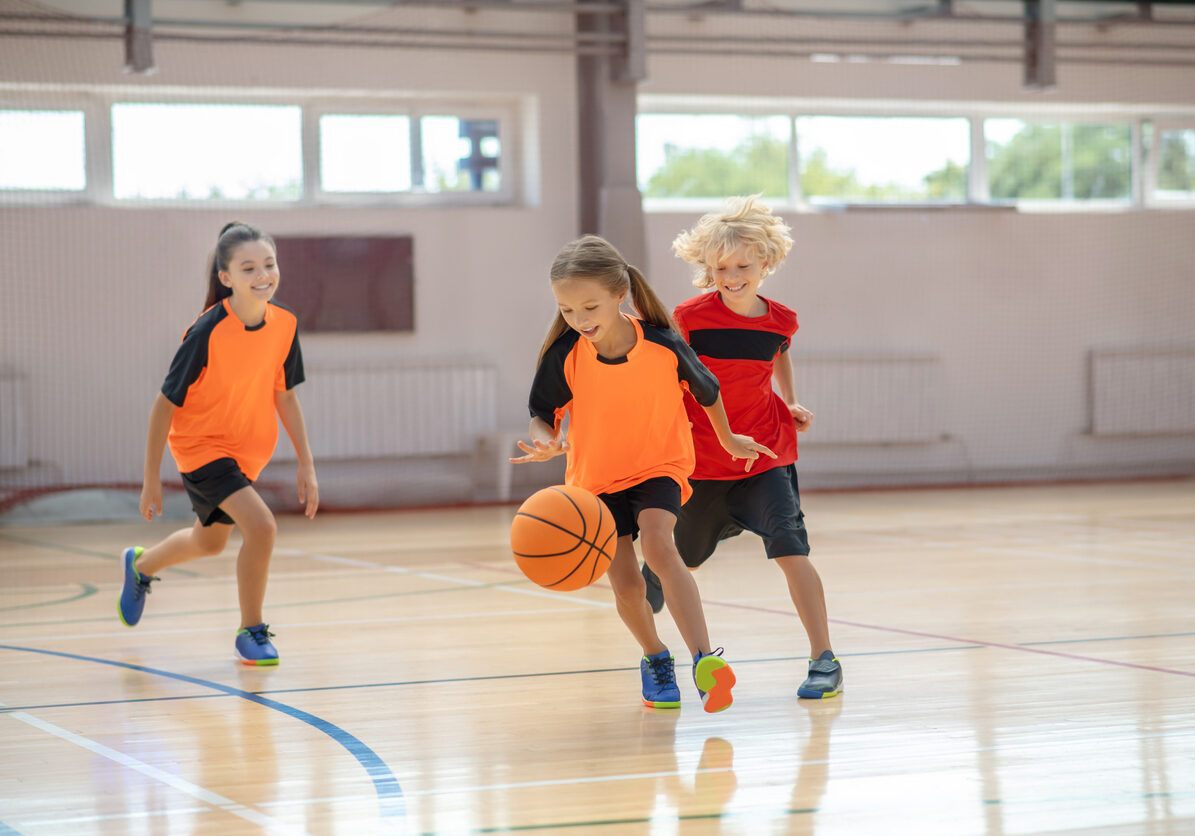 Game. Kids in bright sportswear playing basketball and running after the ball
